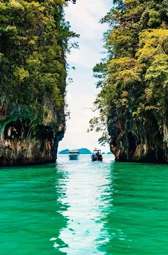 Longtail boats between towering limestone cliffs in the emerald waters of Phang Nga Bay Thailand - Contiki Thai Island Hopping West