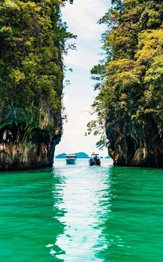 Longtail boats between towering limestone cliffs in the emerald waters of Phang Nga Bay Thailand - Contiki Thai Island Hopping West