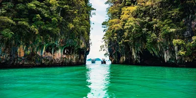 Longtail boats between towering limestone cliffs in the emerald waters of Phang Nga Bay Thailand - Contiki Thai Island Hopping West