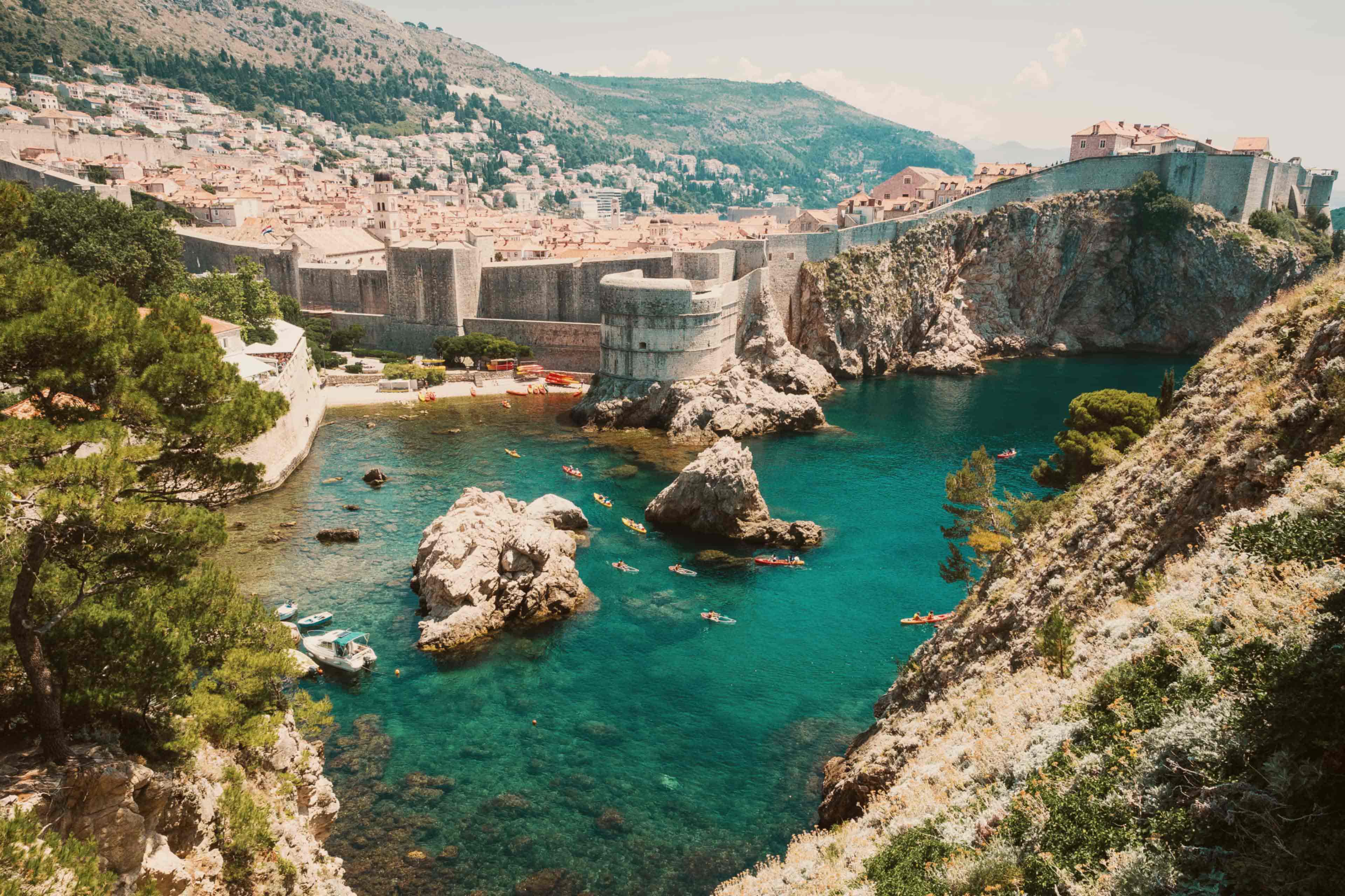 Kayakers paddling in a turquoise cove beneath the old city walls of Dubrovnik, Croatia.
