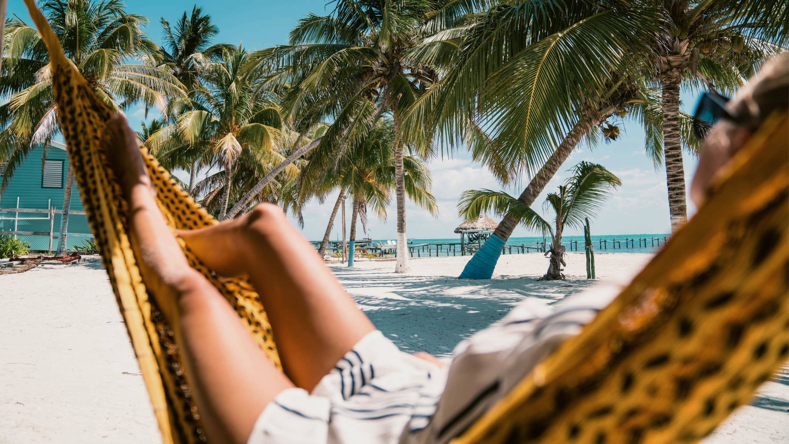 A Contiki traveller relaxing in a hammock beneath swaying palm trees on a tropical Caribbean beach in Belize during the Ultimate Central America Tour