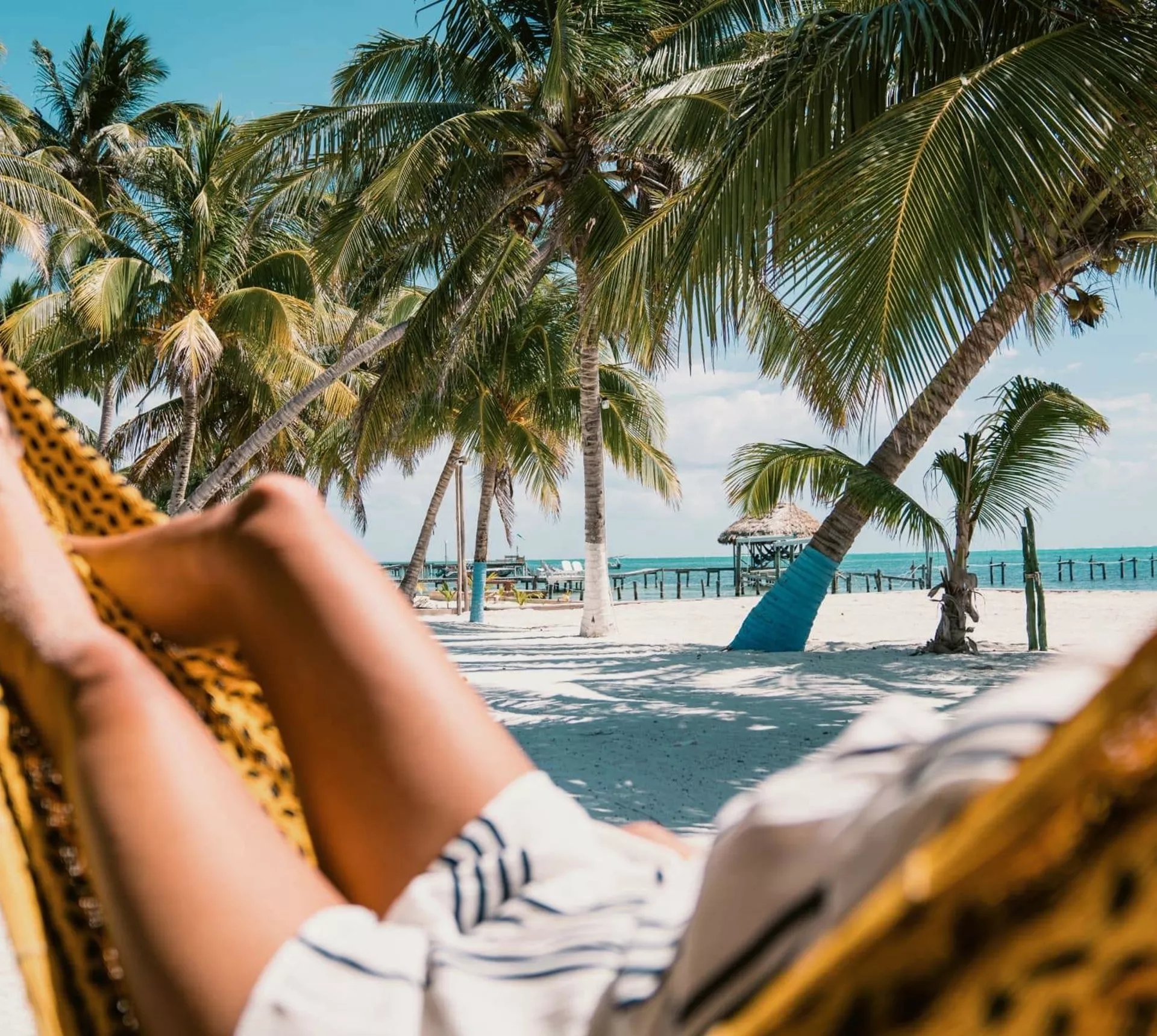 A Contiki traveller relaxing in a hammock beneath swaying palm trees on a tropical Caribbean beach in Belize during the Ultimate Central America Tour