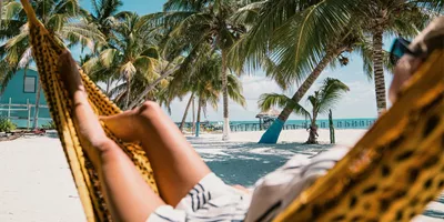 A Contiki traveller relaxing in a hammock beneath swaying palm trees on a tropical Caribbean beach in Belize during the Ultimate Central America Tour