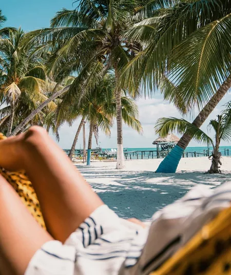 A Contiki traveller relaxing in a hammock beneath swaying palm trees on a tropical Caribbean beach in Belize during the Ultimate Central America Tour