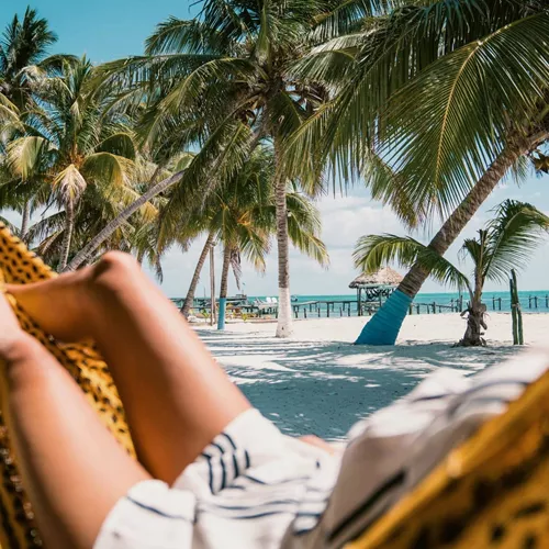 A Contiki traveller relaxing in a hammock beneath swaying palm trees on a tropical Caribbean beach in Belize during the Ultimate Central America Tour