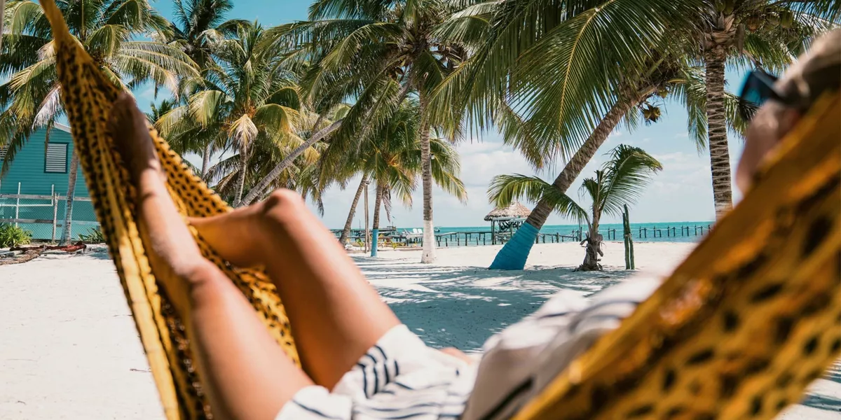 A Contiki traveller relaxing in a hammock beneath swaying palm trees on a tropical Caribbean beach in Belize during the Ultimate Central America Tour