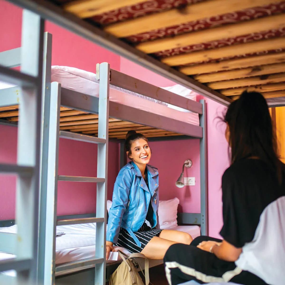 Girls chatting while sitting on beds in pink bedroom in  Plus Hostel Berlin
