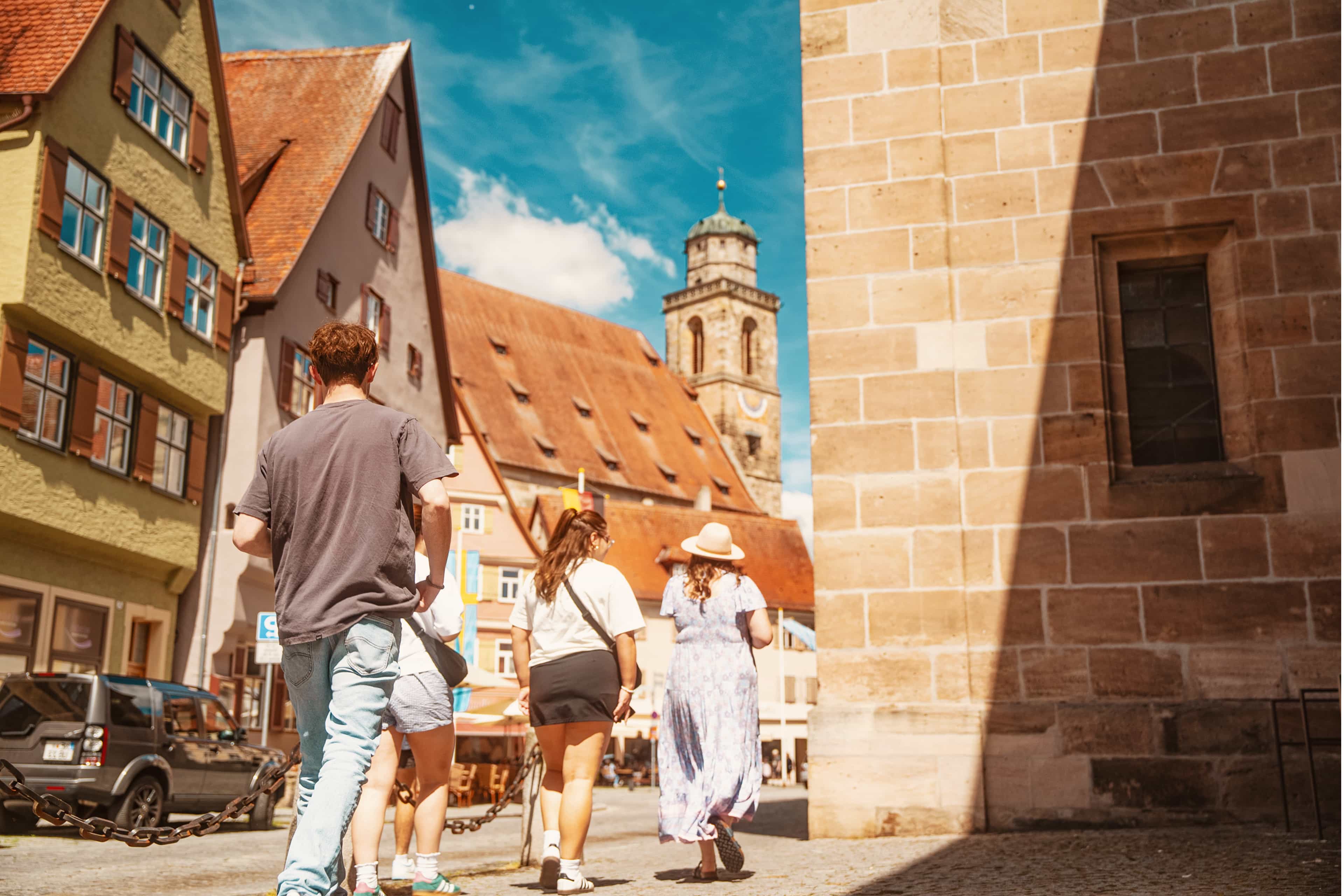 Travellers walking through a picturesque old town square towards a church tower in Germany.