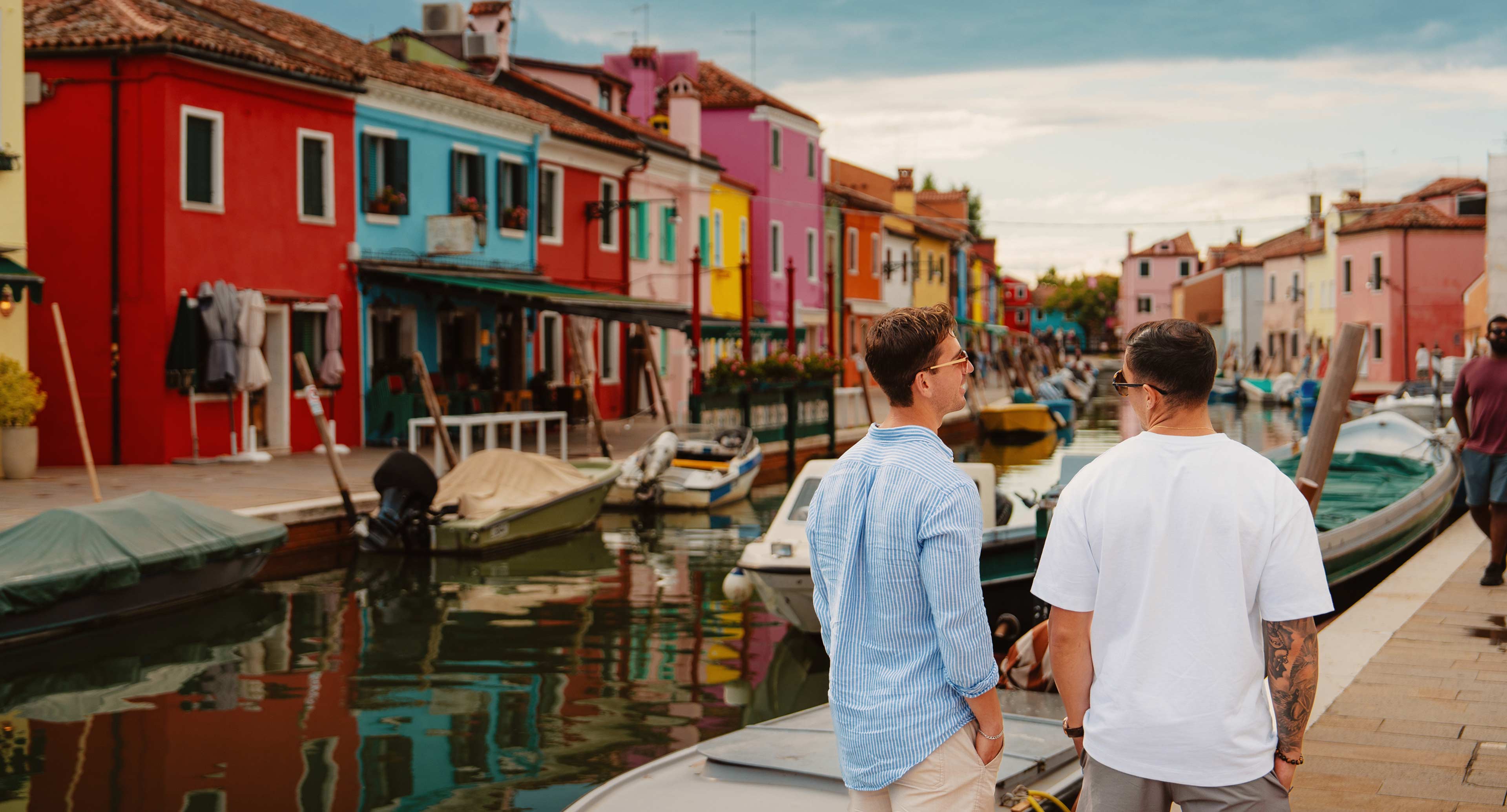 Travellers strolling canal colourful houses boats in burano, italy