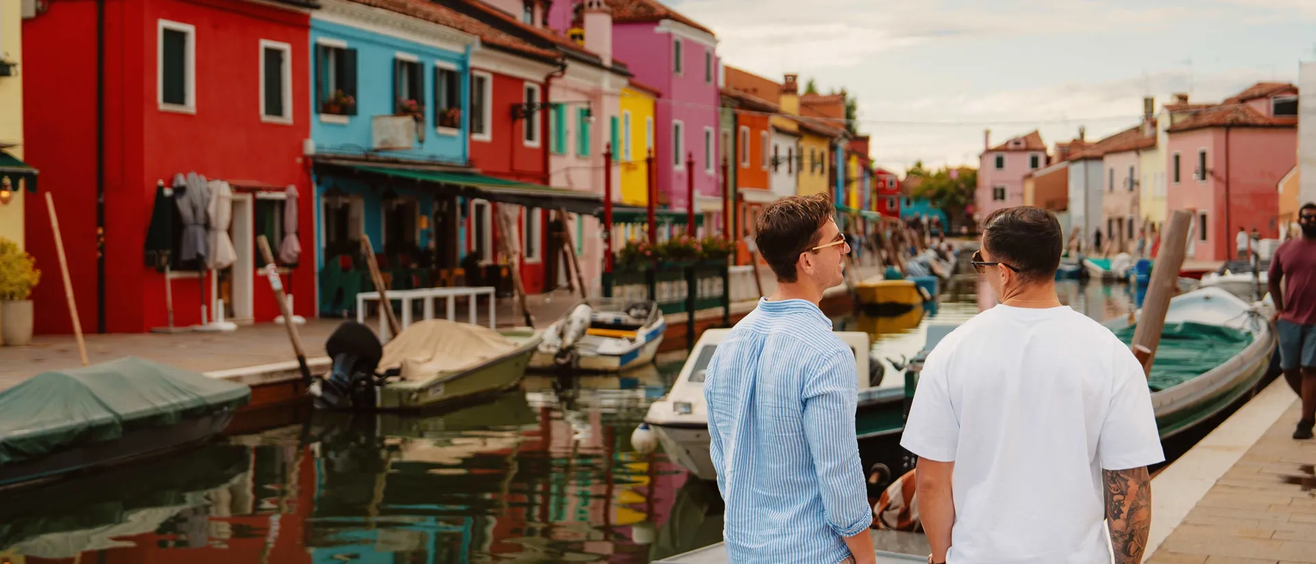 Travellers strolling canal colourful houses boats in burano, italy