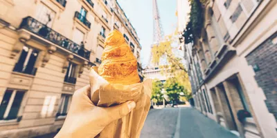 A freshly baked croissant held up towards the Eiffel Tower on a quiet Paris street during the Contiki European Horizon Tour