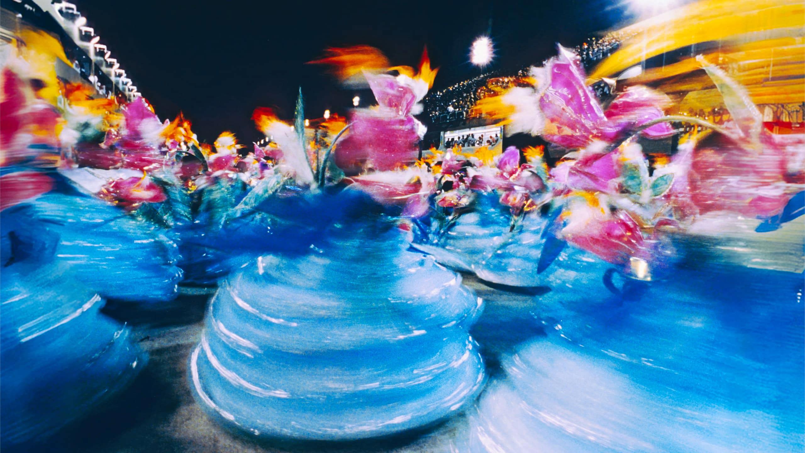 Motion-blurred samba dancers in vibrant blue and pink carnival costumes at the Sambadrome Rio Carnival Brazil - Contiki Brazil Tour
