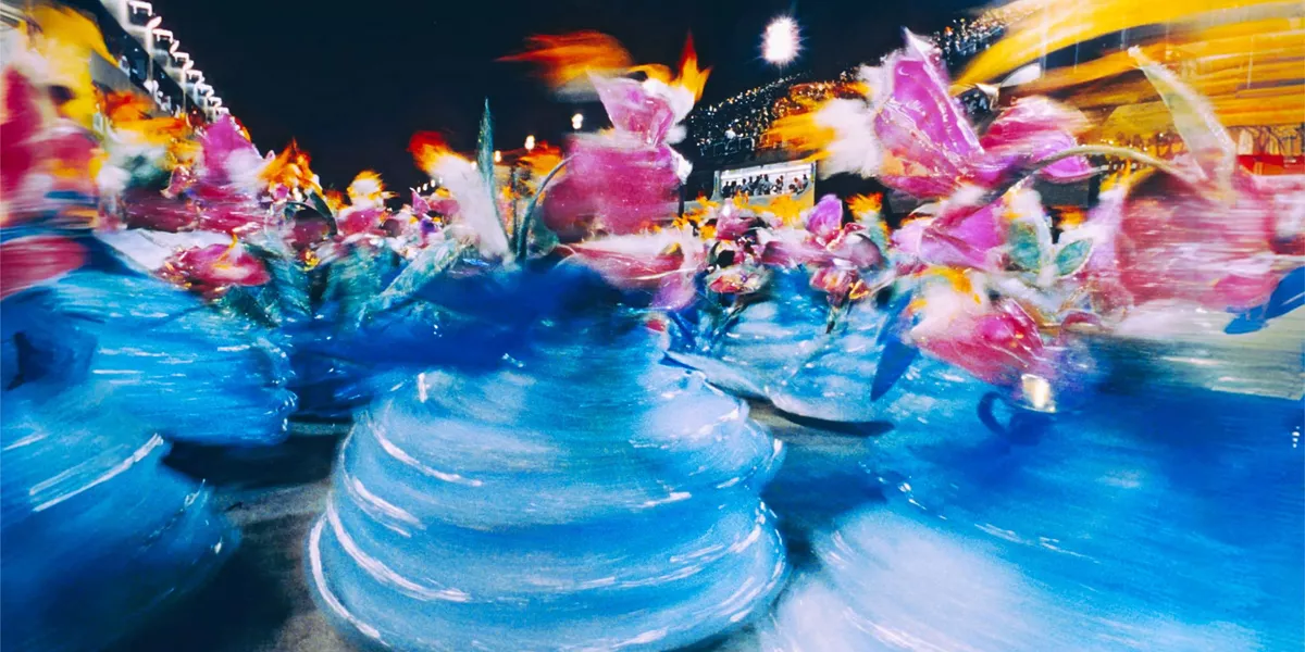 Colourful Carnival performers in elaborate costumes spin through a parade during Carnival celebrations in Brazil at night