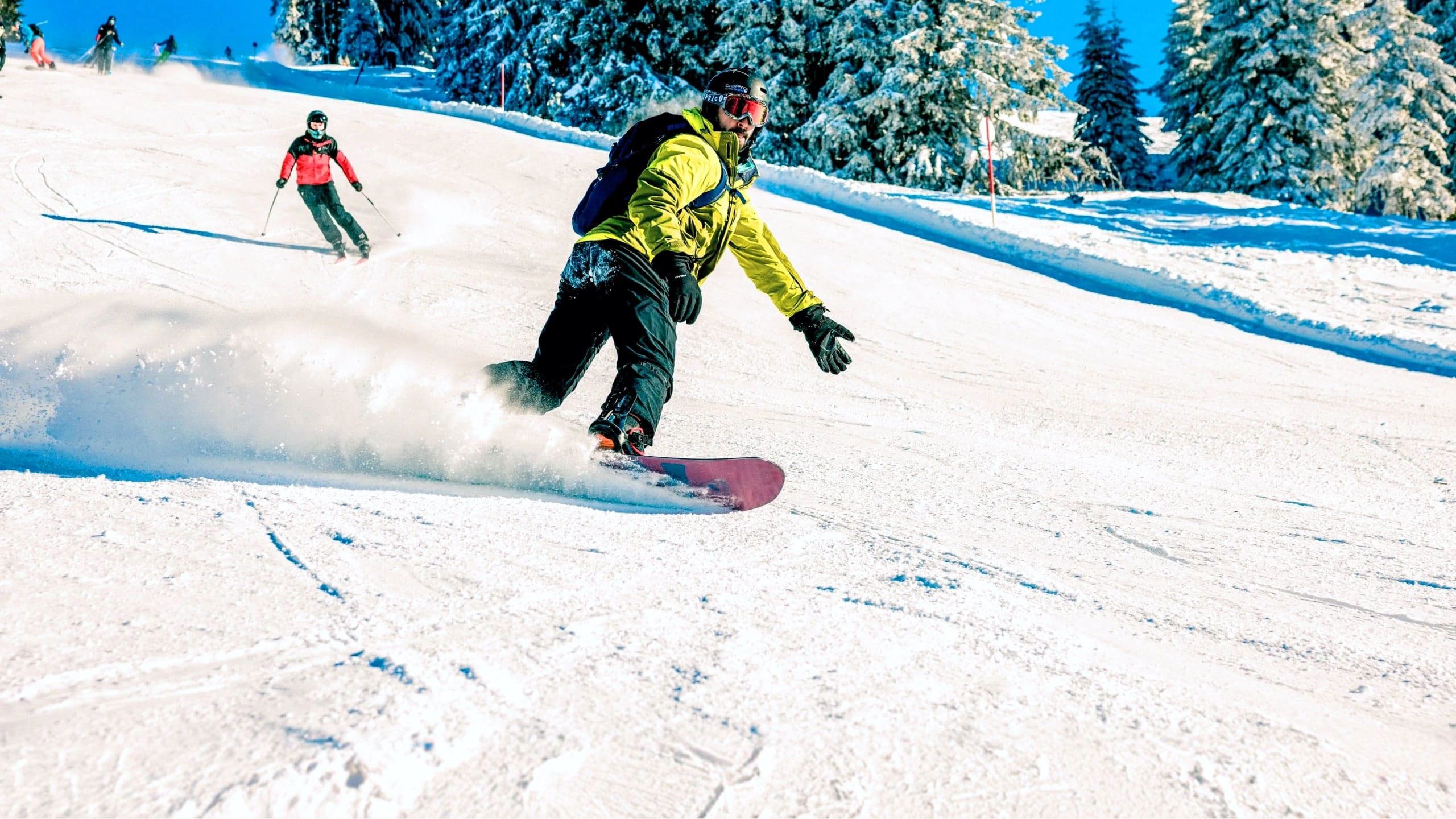 A snowboarder carves down a snowy slope in the Austrian Alps, with skiers following behind on a clear winter day