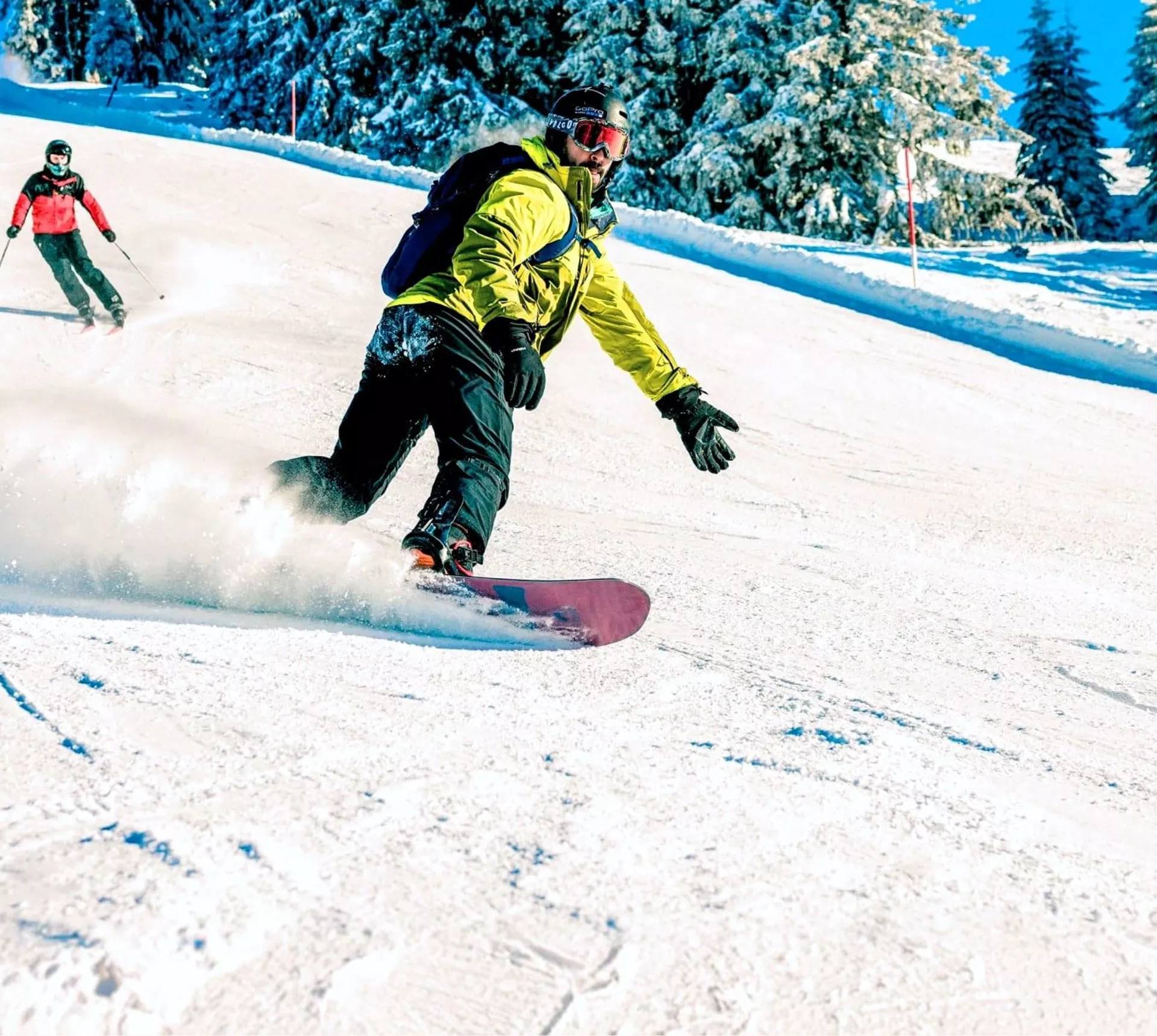 A snowboarder carves down a snowy slope in the Austrian Alps, with skiers following behind on a clear winter day