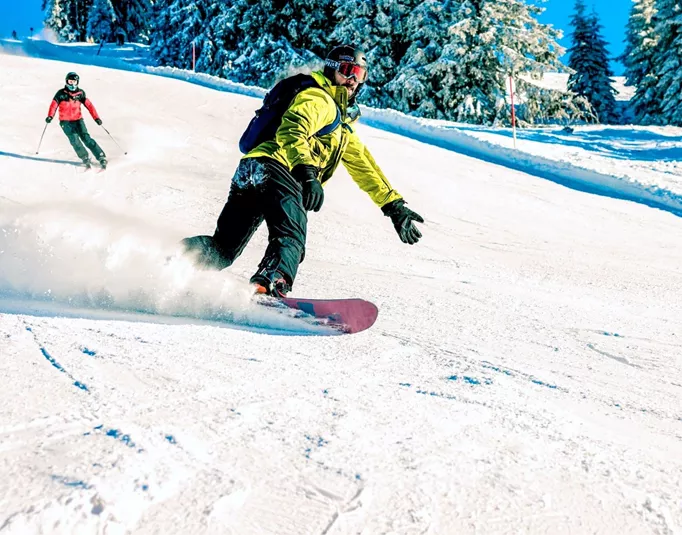 A snowboarder carves down a snowy slope in the Austrian Alps, with skiers following behind on a clear winter day