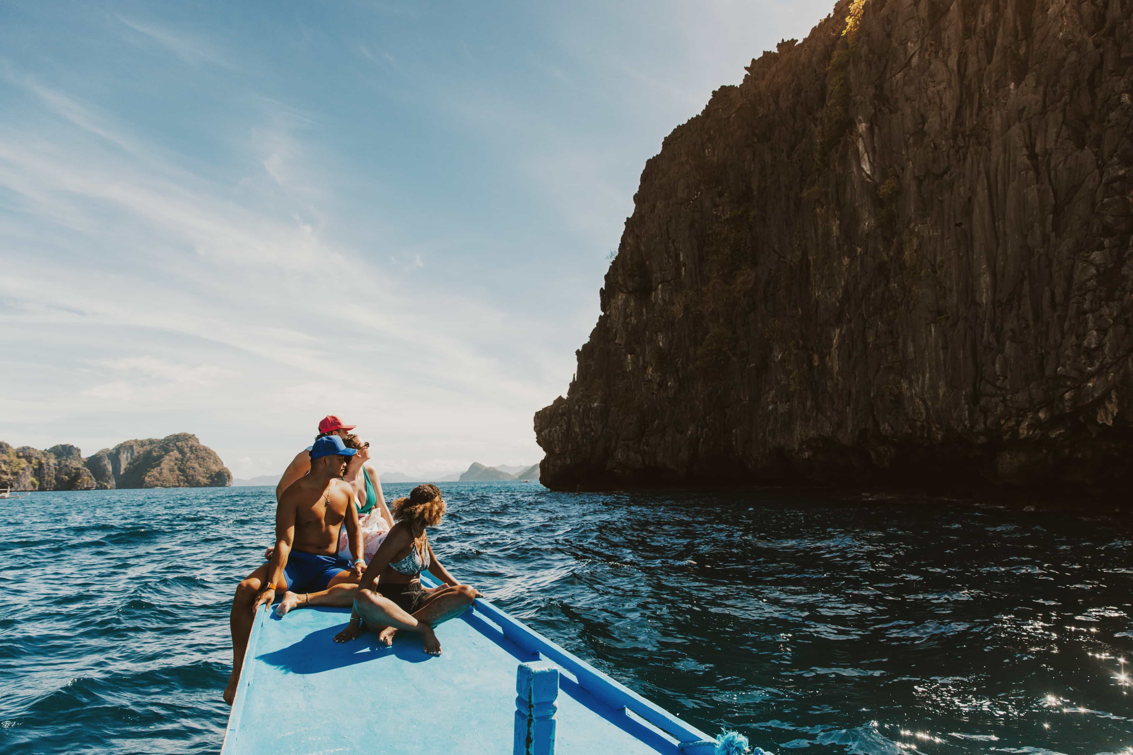 Travellers relax on the bow of a boat cruising past dramatic limestone cliffs and islands in Palawan, Philippines.