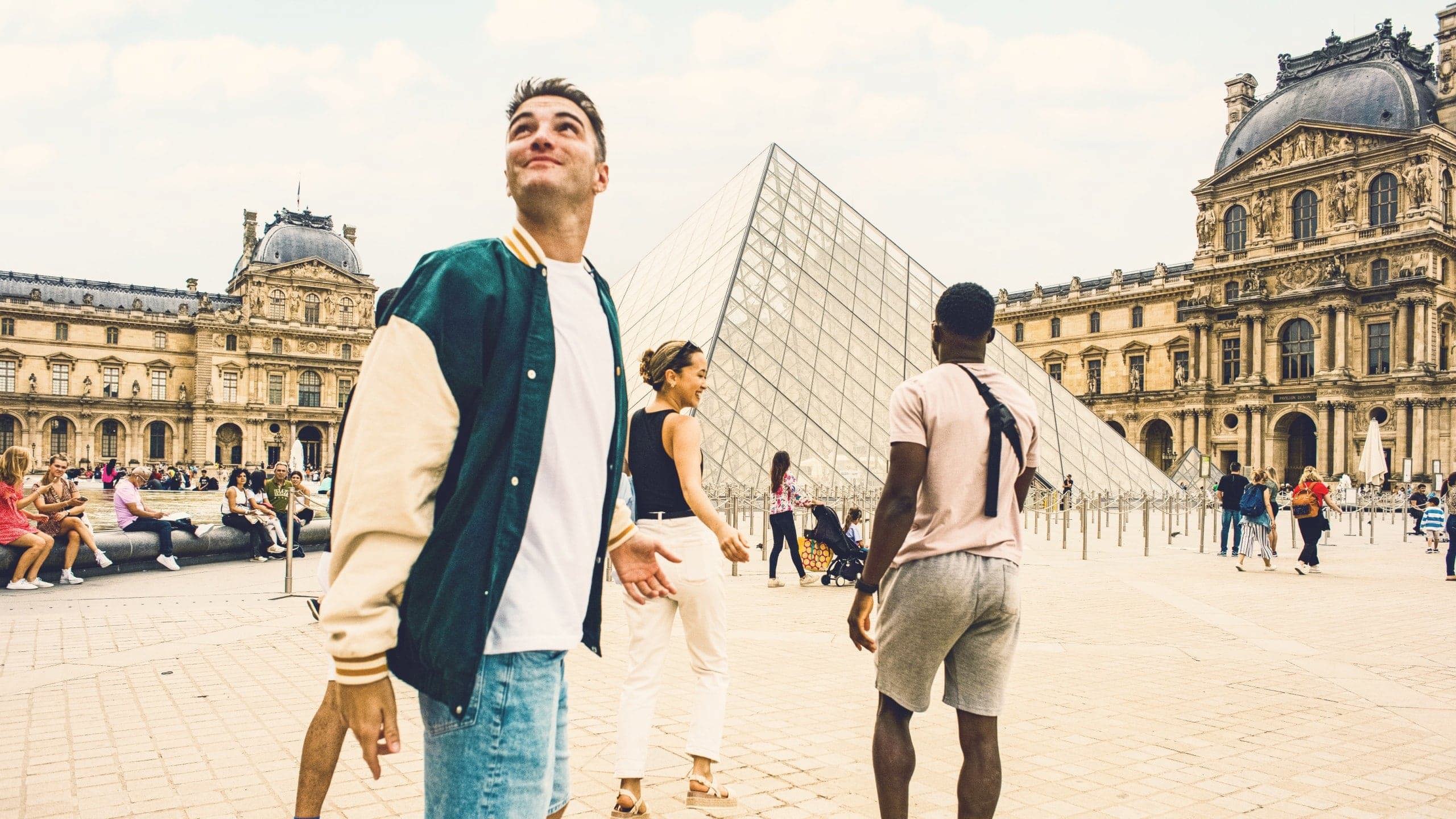 Contiki travellers explore the Louvre Museum courtyard in Paris, with the iconic glass pyramid at the heart of the scene, on the London to Rome Tour