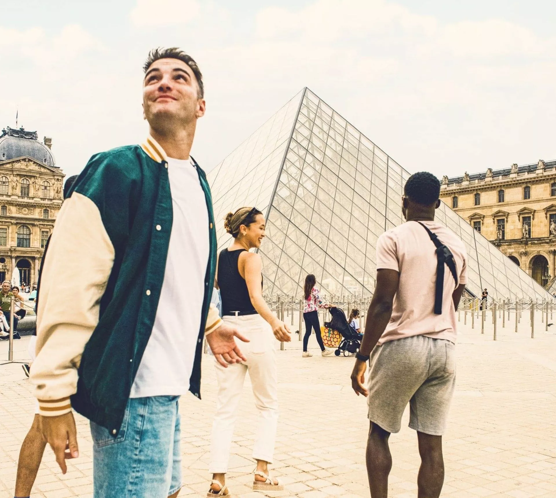 Contiki travellers explore the Louvre Museum courtyard in Paris, with the iconic glass pyramid at the heart of the scene, on the London to Rome Tour