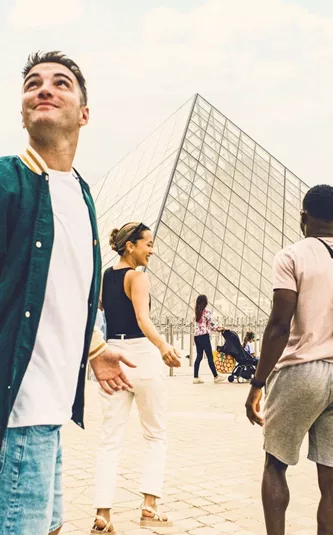 Contiki travellers explore the Louvre Museum courtyard in Paris, with the iconic glass pyramid at the heart of the scene, on the London to Rome Tour