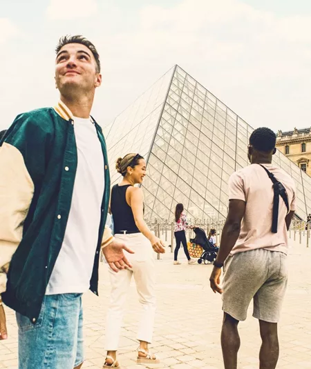 Contiki travellers explore the Louvre Museum courtyard in Paris, with the iconic glass pyramid at the heart of the scene, on the London to Rome Tour