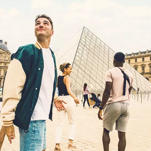 Contiki travellers explore the Louvre Museum courtyard in Paris, with the iconic glass pyramid at the heart of the scene, on the London to Rome Tour