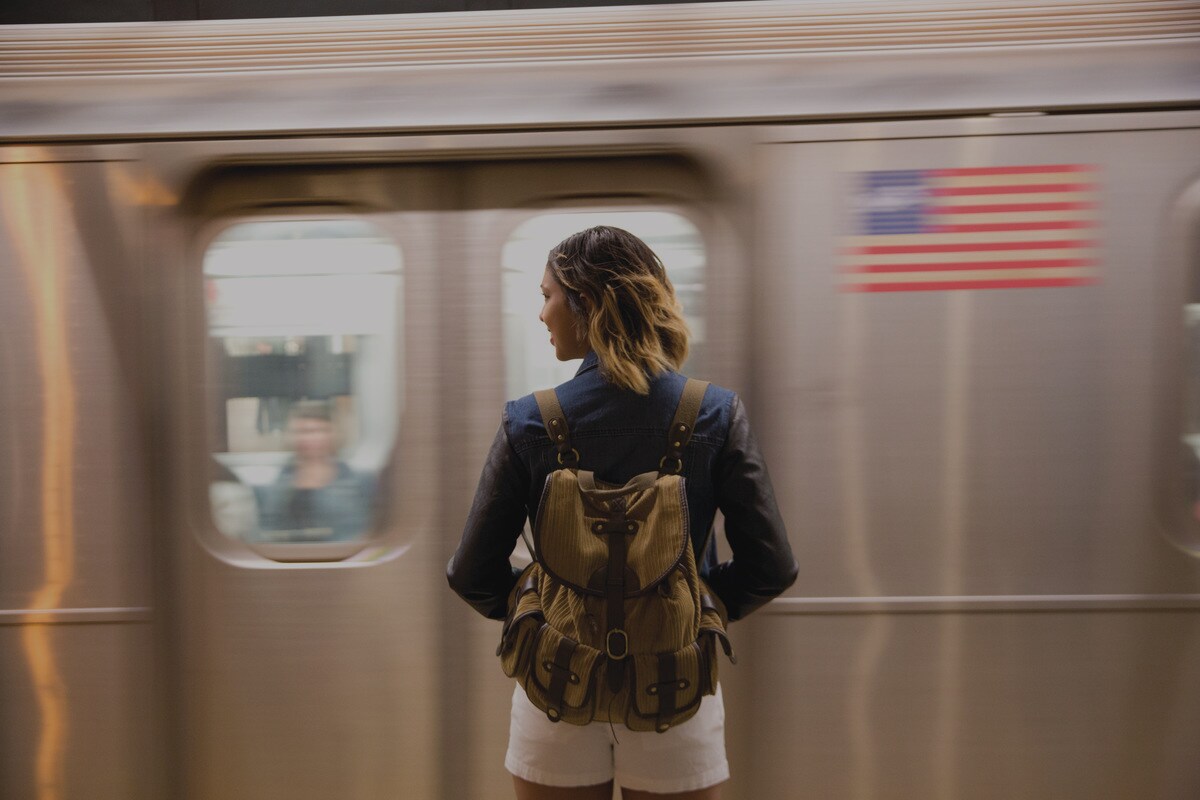 Woman with a backpack standing in front of underground train with American flag on the side