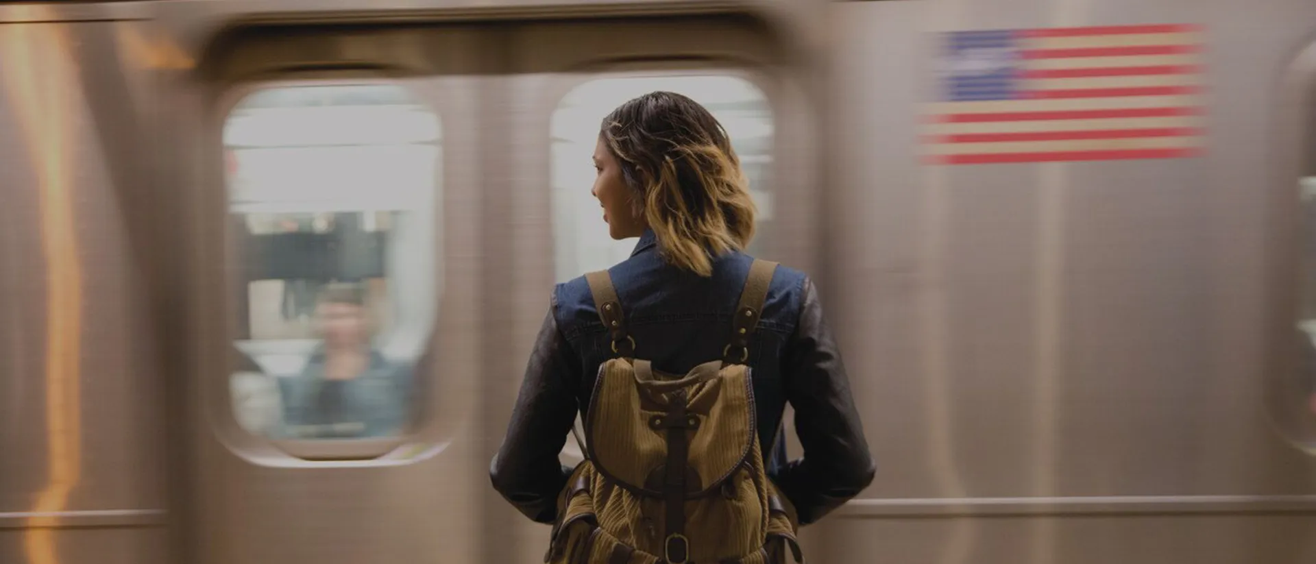 Woman with a backpack standing in front of underground train with American flag on the side
