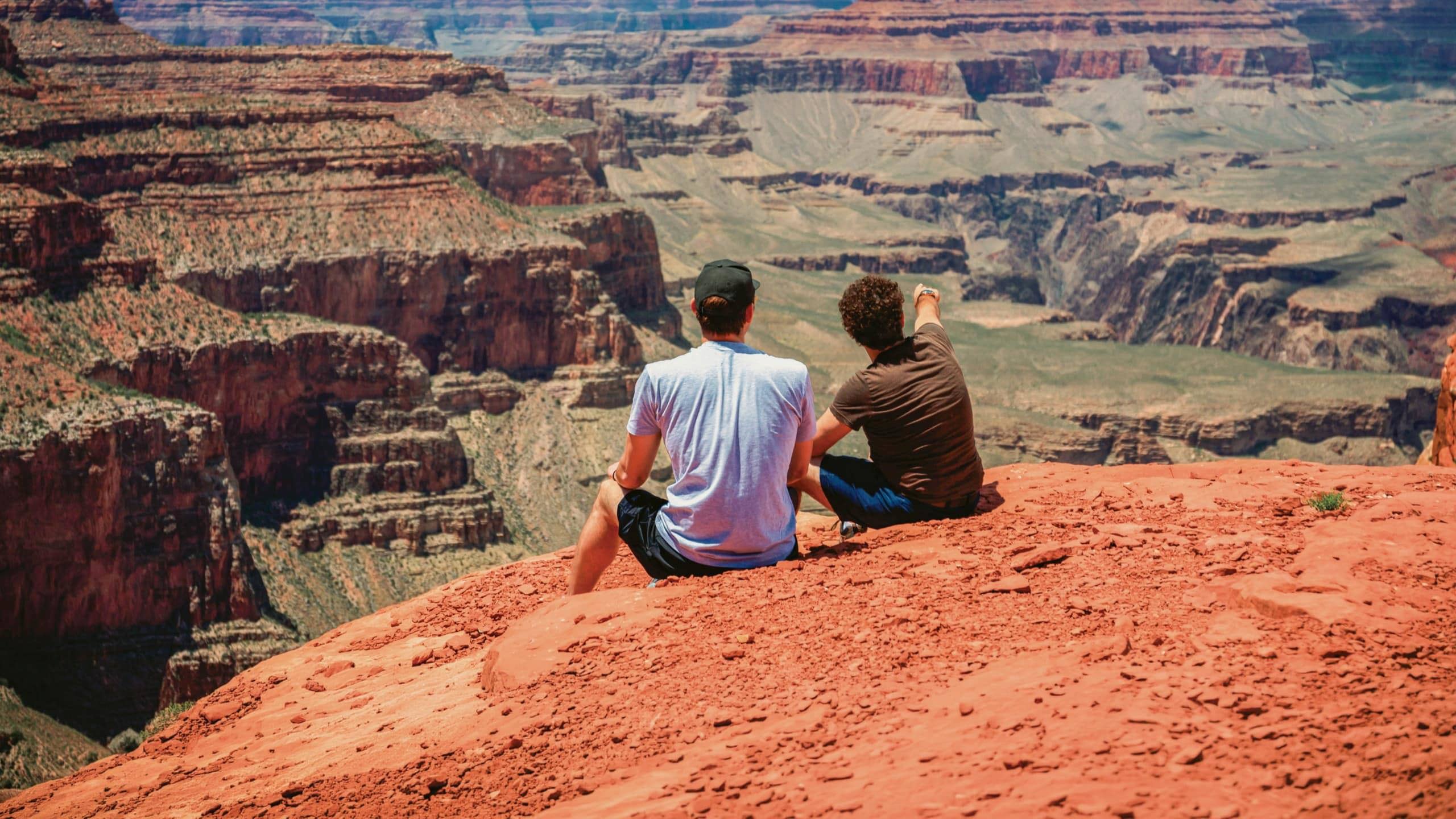 Two Contiki travellers overlooking the Grand Canyon National Park, taking in panoramic views of the iconic red rock cliffs on the Los Angeles to Dallas Tour