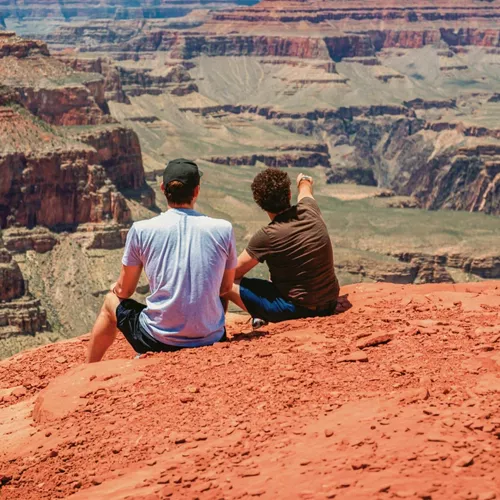 Two Contiki travellers overlooking the Grand Canyon National Park, taking in panoramic views of the iconic red rock cliffs on the Los Angeles to Dallas Tour
