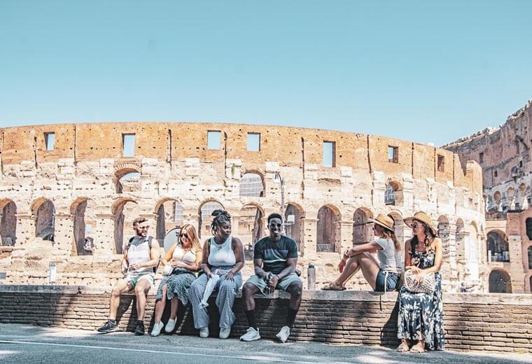 Travellers sitting on a wall in front of Colloseum in Rome