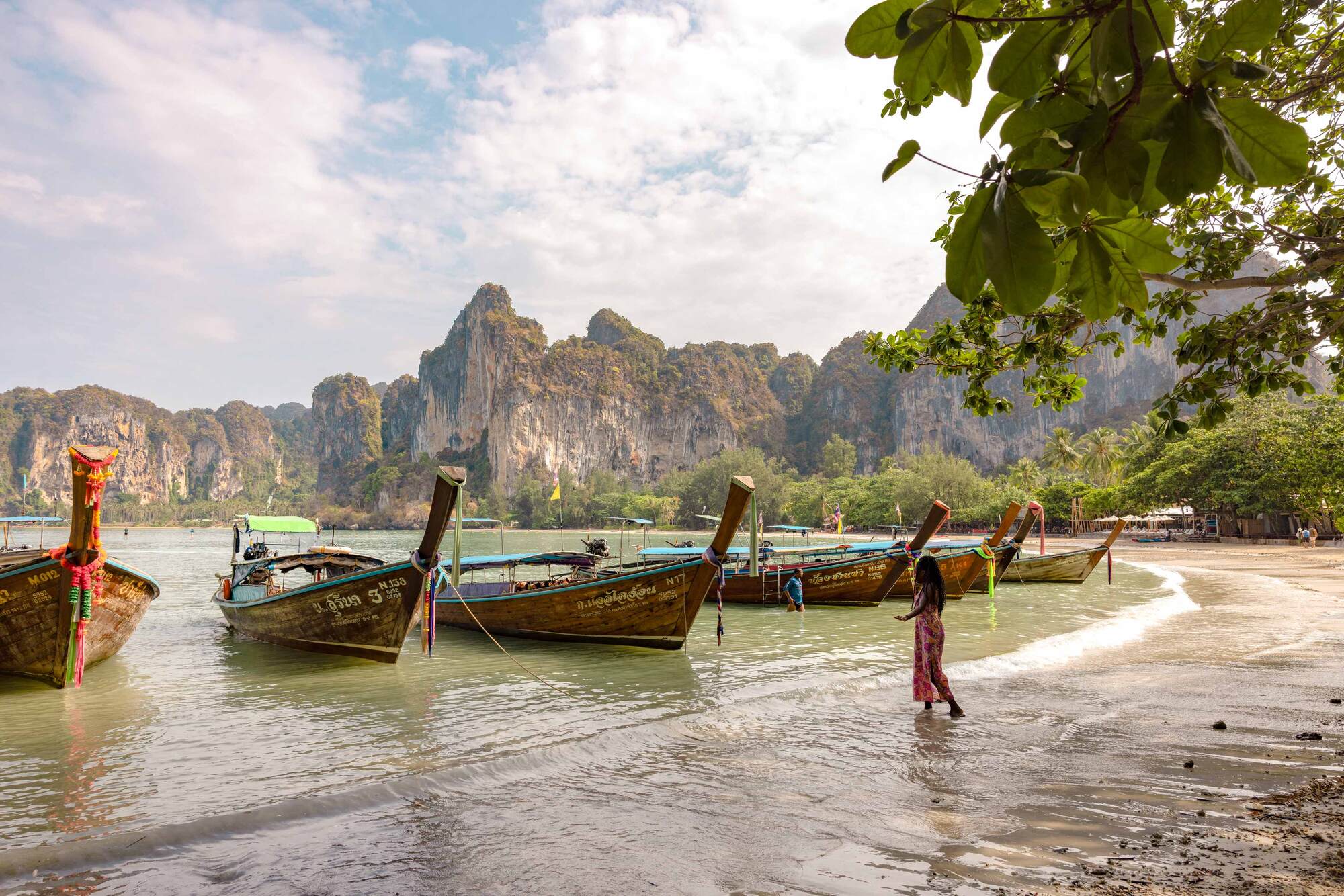 A woman standing near traditional Thai long-tail boats in Thailand