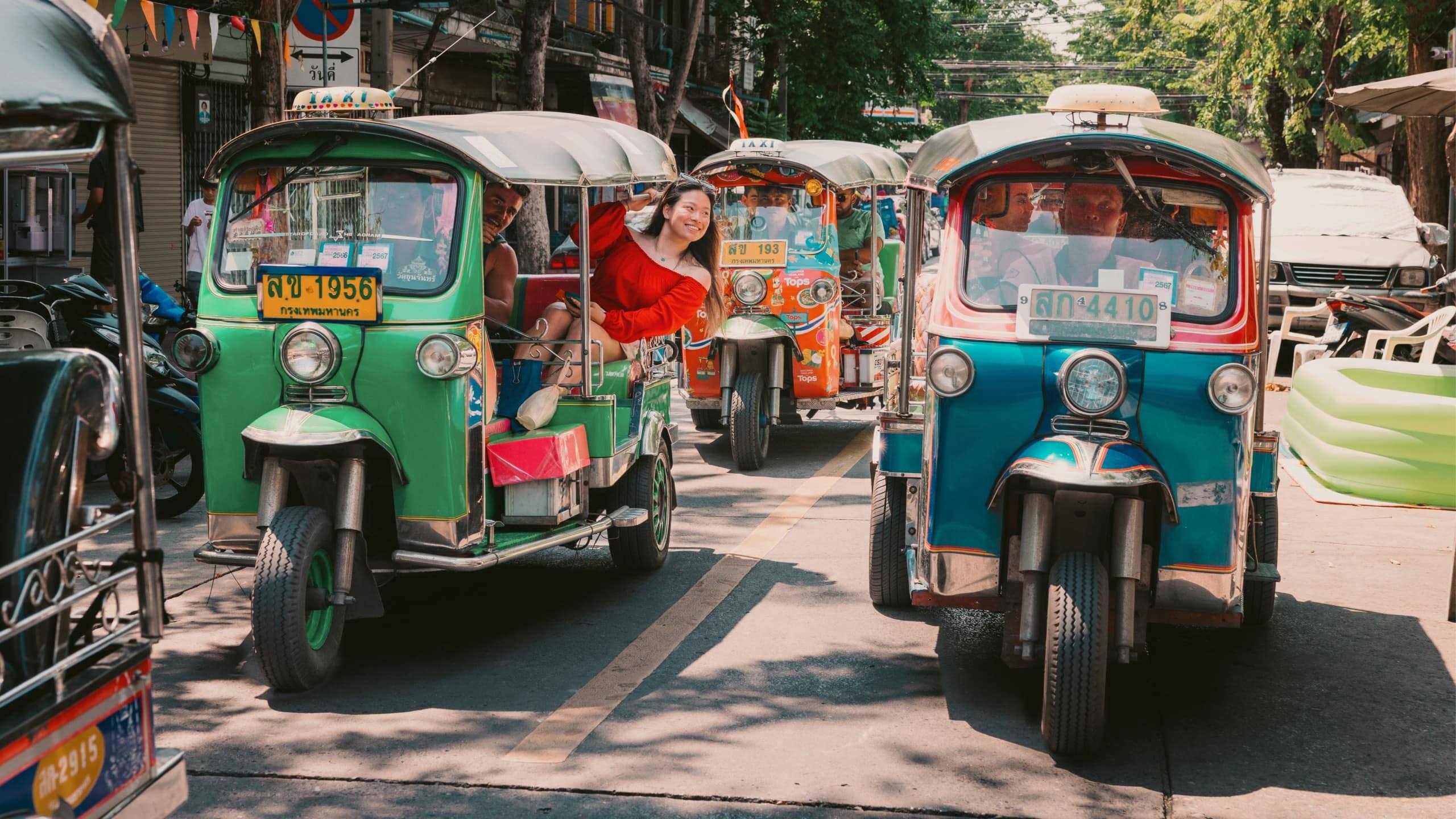 Travellers ride colourful tuk-tuks through the streets of Bangkok on the Contiki Best of Thailand Tour