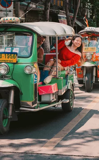 Travellers ride colourful tuk-tuks through the streets of Bangkok on the Contiki Best of Thailand Tour