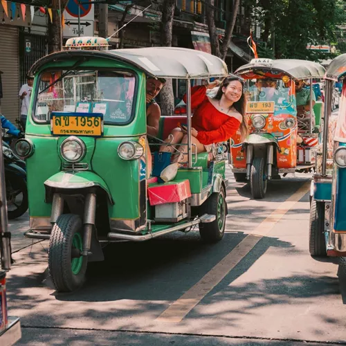 Travellers ride colourful tuk-tuks through the streets of Bangkok on the Contiki Best of Thailand Tour