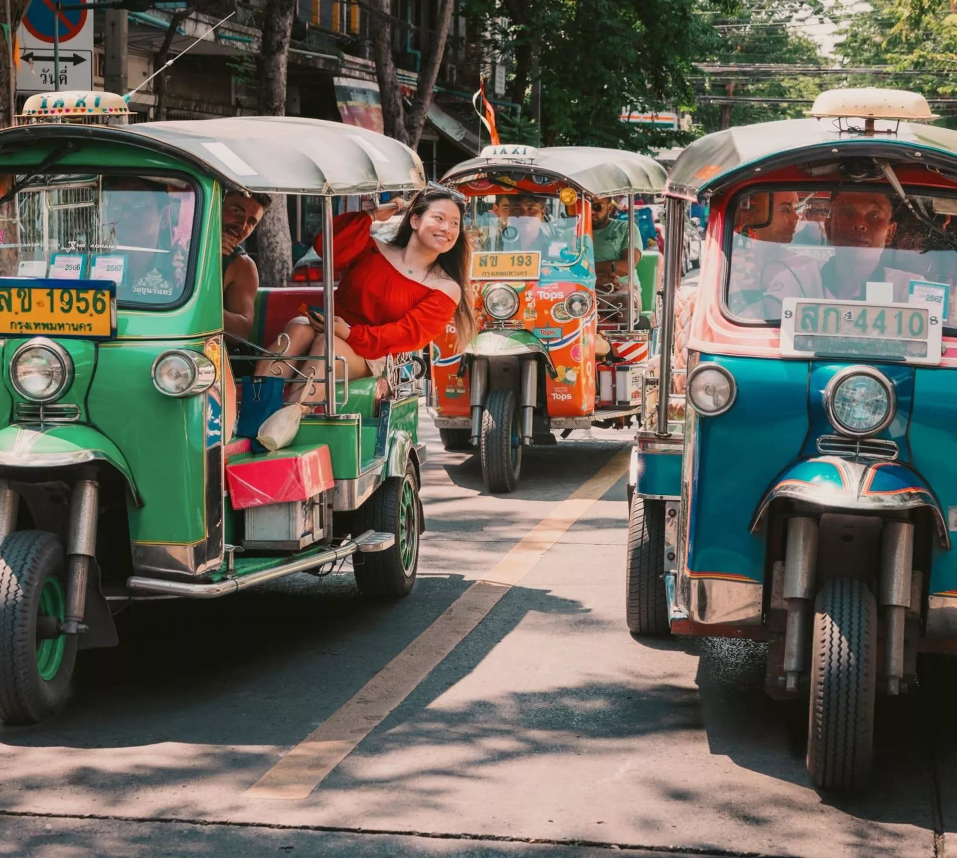 Travellers ride colourful tuk-tuks through the streets of Bangkok on the Contiki Best of Thailand Tour