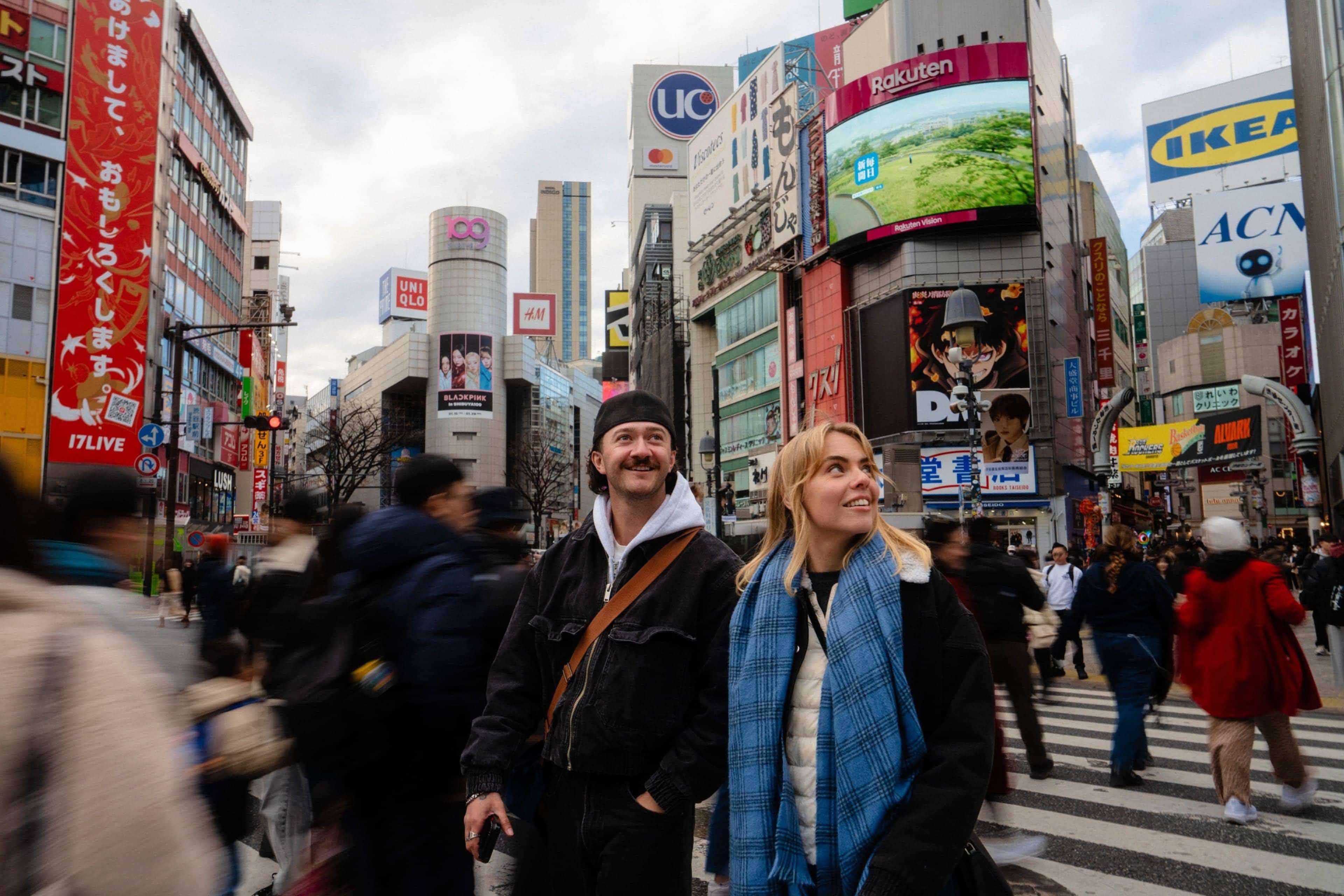 Travellers crossing Shibuya Crossing in Tokyo, Japan, surrounded by colourful billboards and city lights.
