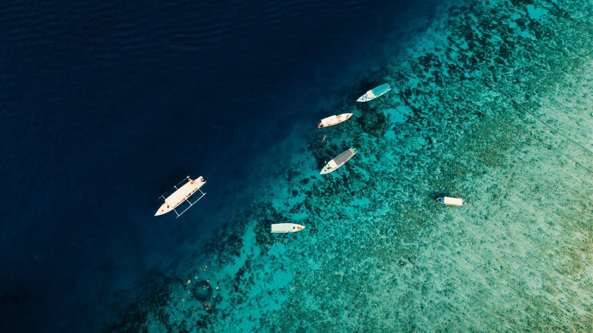 Aerial drone view of boats and snorkellers over a vivid turquoise coral reef drop-off in Bali Indonesia - Contiki Bali Island Hopping Tour