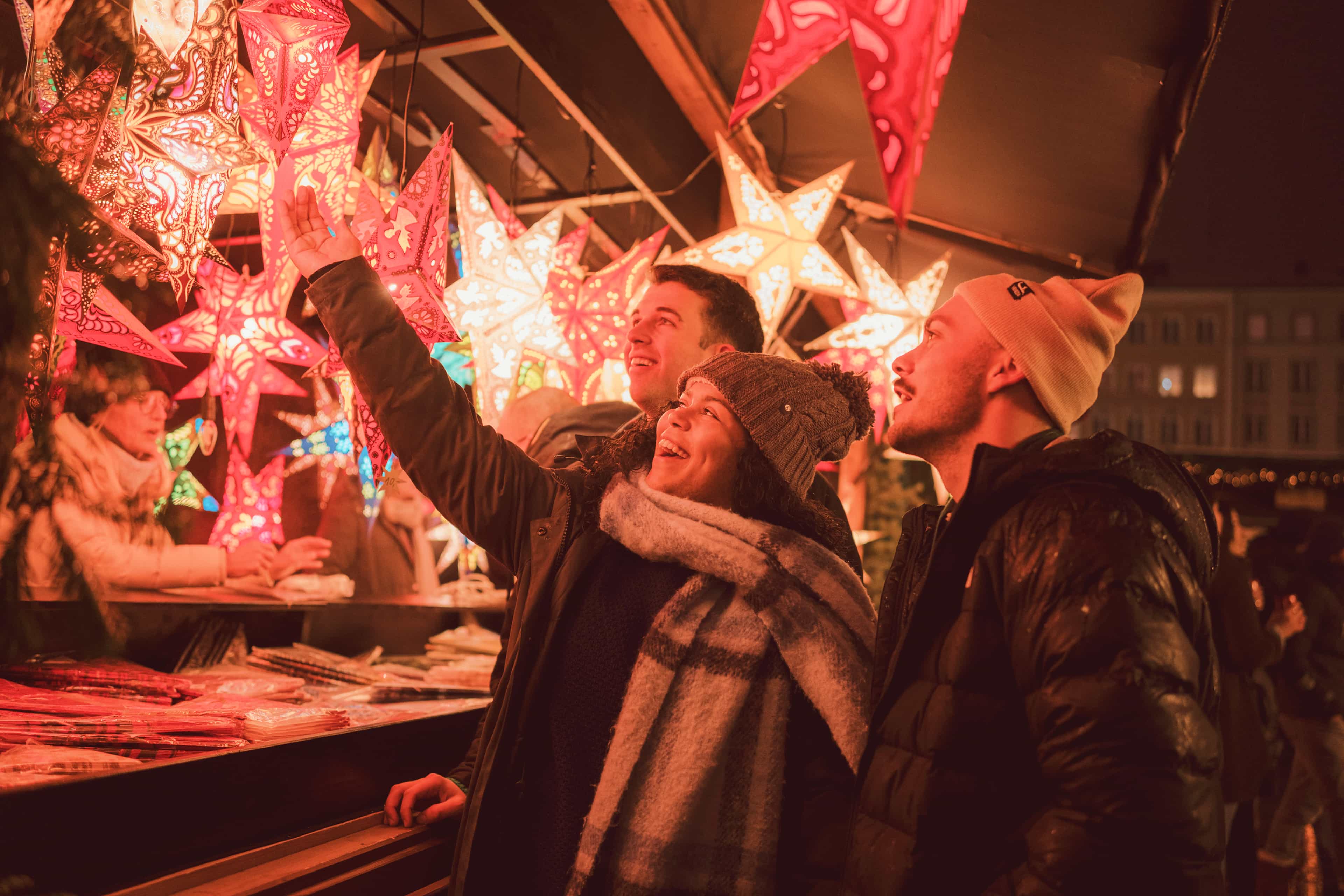 Travellers admiring illuminated star lanterns at a Christmas market stall in Germany.
