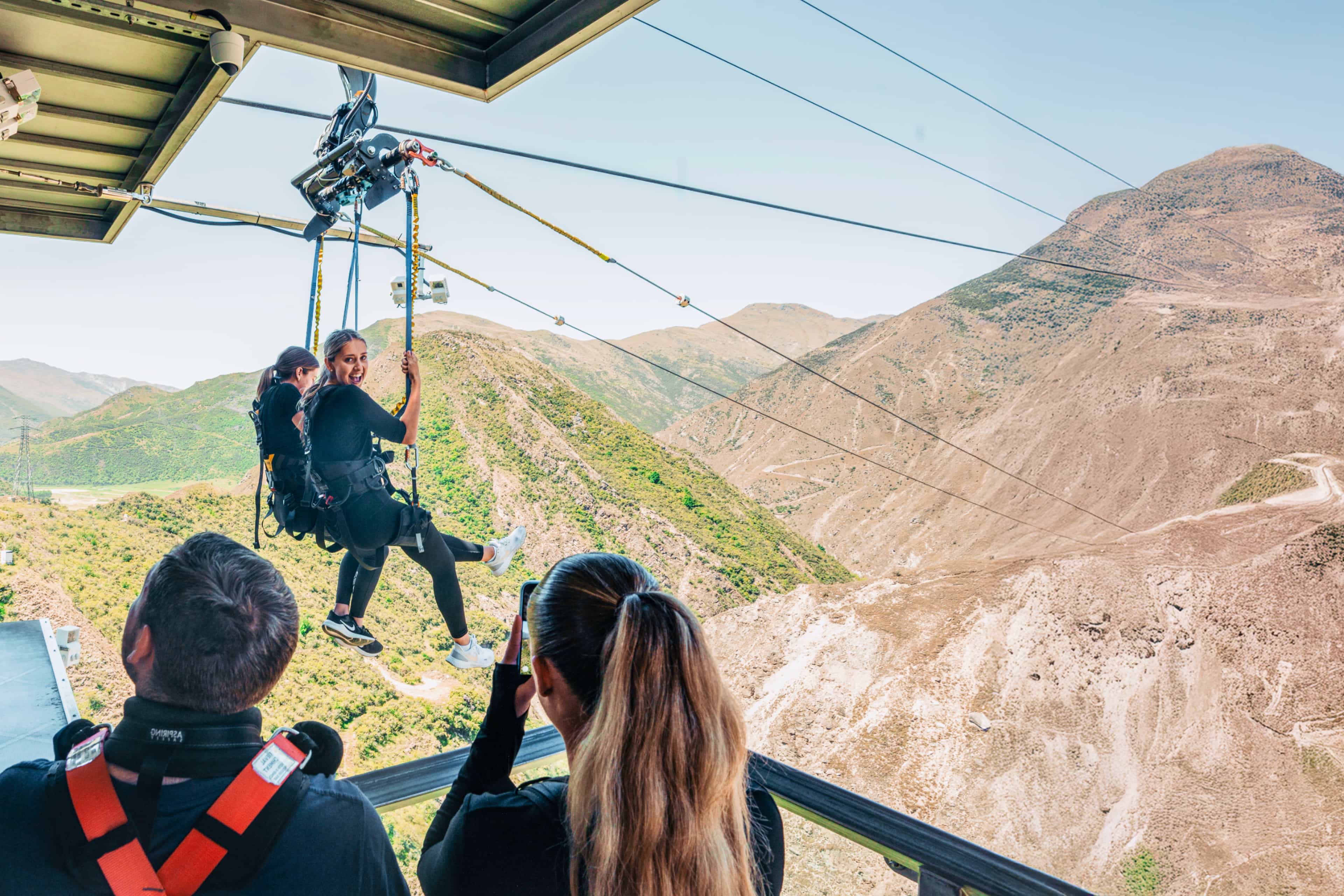 Travellers launch off a high-altitude zipline over dramatic mountain terrain in Queenstown, New Zealand.