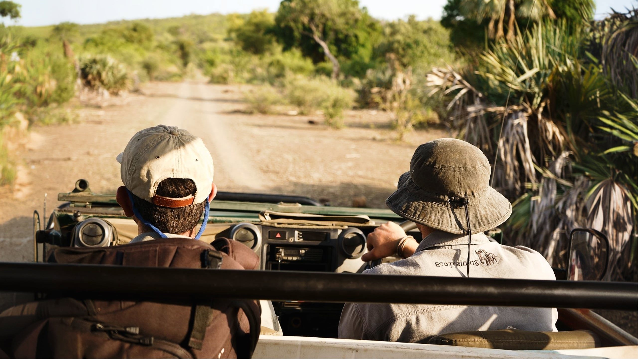 Two people drive through the bush in an open safari vehicle during a game drive in South Africa's Greater Kruger region - Contiki Become a Safari Guide in Kruger Tour