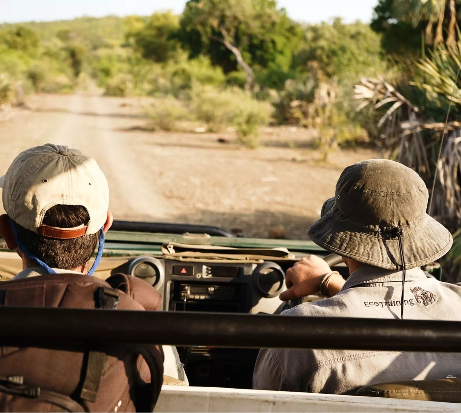Two people drive through the bush in an open safari vehicle during a game drive in South Africa's Greater Kruger region - Contiki Become a Safari Guide in Kruger Tour