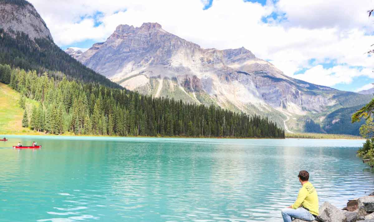 Man Sitting At The Edge Of A Lake Looking At The Mountains