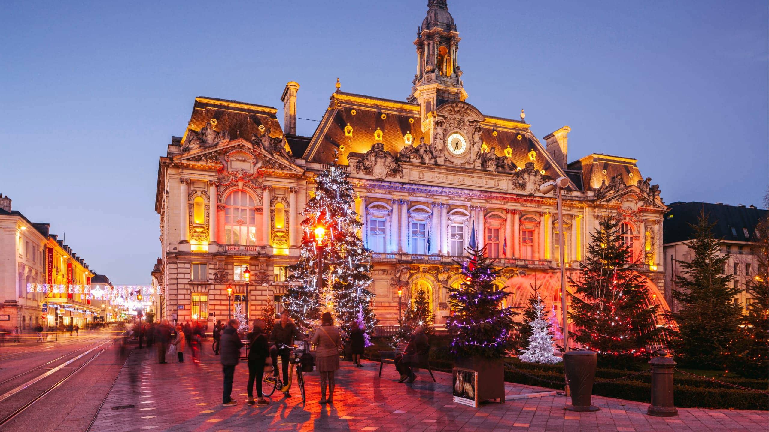 Contiki travellers exploring a stunning Christmas market square in Paris with a illuminated baroque town hall and decorated Christmas trees at twilight
