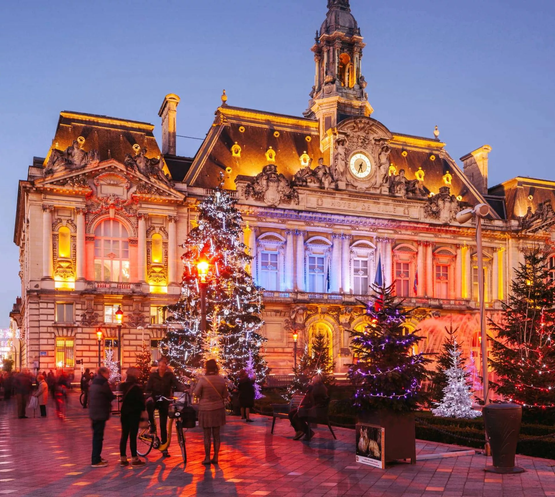 Contiki travellers exploring a stunning Christmas market square in Paris with a illuminated baroque town hall and decorated Christmas trees at twilight