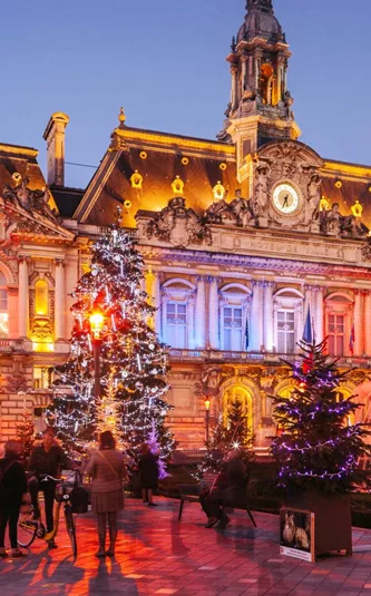Contiki travellers exploring a stunning Christmas market square in Paris with a illuminated baroque town hall and decorated Christmas trees at twilight