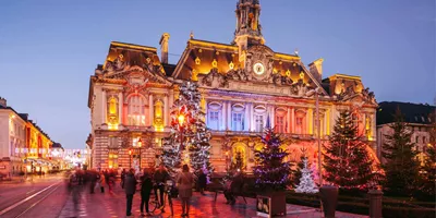 Contiki travellers exploring a stunning Christmas market square in Paris with a illuminated baroque town hall and decorated Christmas trees at twilight
