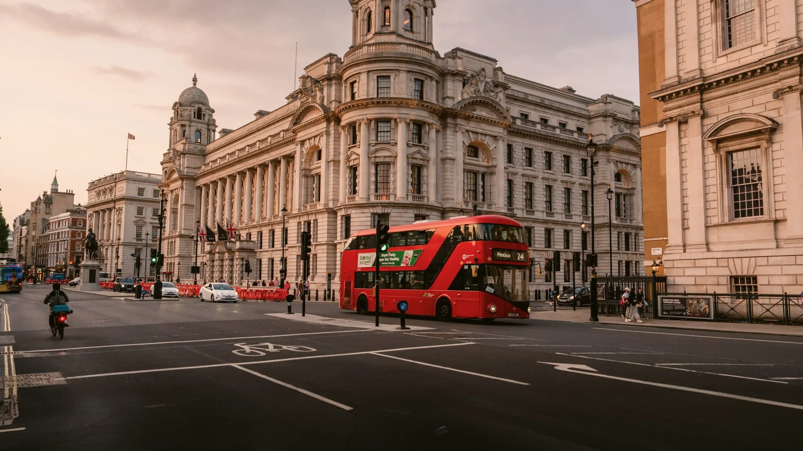 A classic red double-decker bus travels through central London at sunset on the Contiki London Mini Break