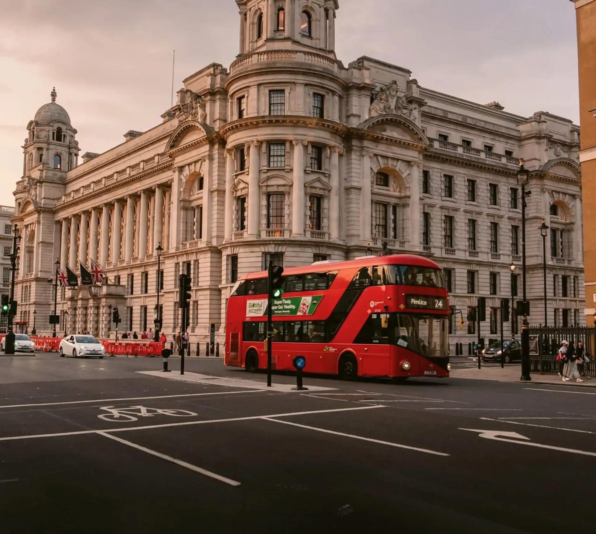 A classic red double-decker bus travels through central London at sunset on the Contiki London Mini Break