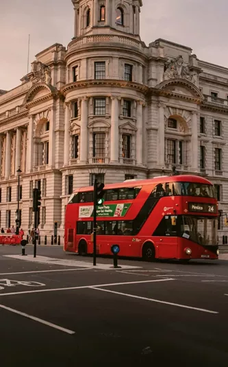 A classic red double-decker bus travels through central London at sunset on the Contiki London Mini Break